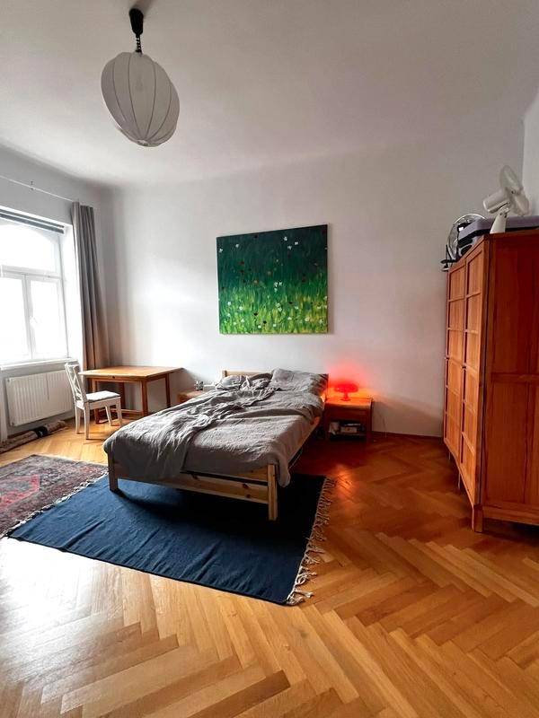 Gemütliches Schlafzimmer mit Holzbett, Kleiderschrank und Schreibtisch, hell durch großes Fenster.