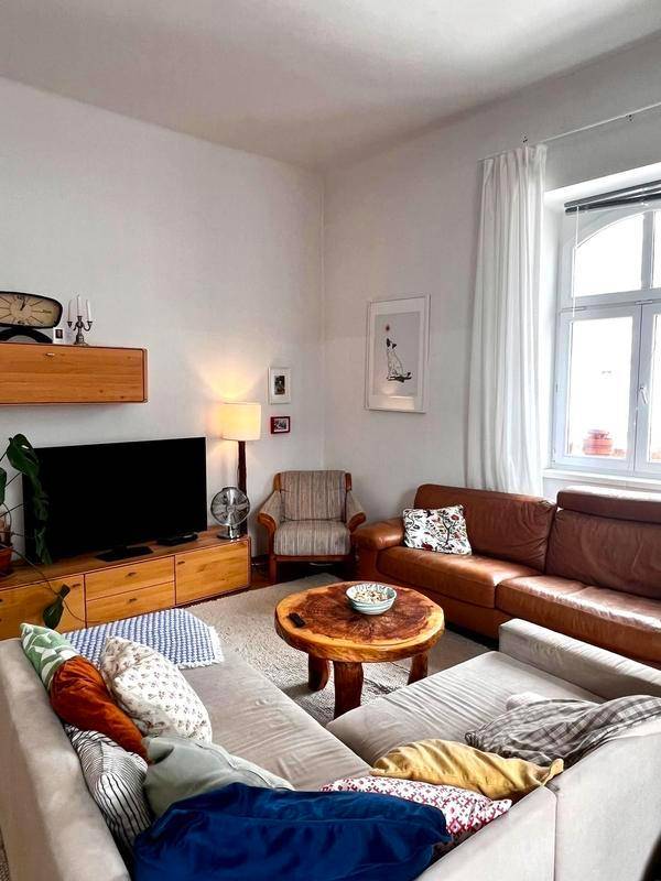 Gemütliche Wohnecke mit beigem Sofa, Holztisch und Fernsehmöbeln, beleuchtet durch ein Fenster.