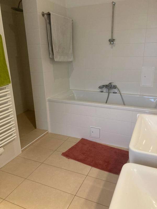 Helles Badezimmer mit Badewanne, Dusche und zwei Waschbecken auf hellen Fliesen.