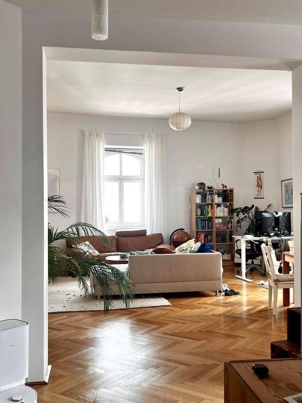 Helles Wohnzimmer mit Fischgrätparkett, bequemen Sofas und einem Arbeitsbereich am Fenster.