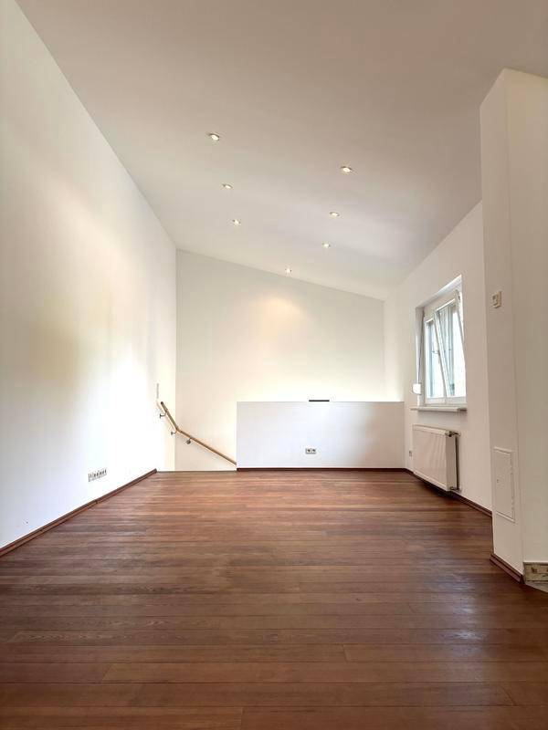 Heller, leerer Wohnbereich mit Holzboden, hohen Decken und Dachschräge.