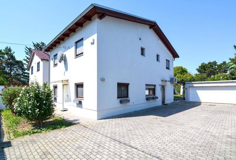 Weiß verputztes Einfamilienhaus mit Satteldach und gepflasterter Auffahrt.