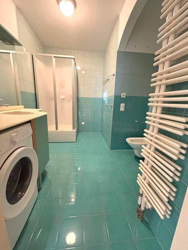 Badezimmer mit türkisblauen Fliesen, Duschkabine, WC und Waschmaschine.