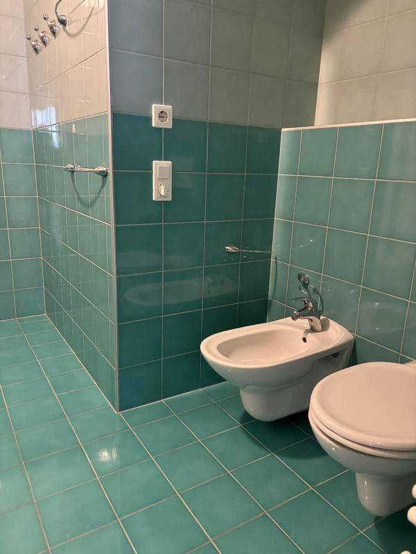 Badezimmer mit türkisblauen Fliesen, ausgestattet mit Bidet und WC.