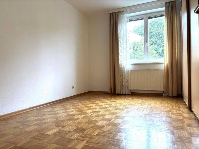 Leeres Schlafzimmer mit Parkettboden, Fenster und Heizkörper, bereit zur individuellen Gestaltung.
