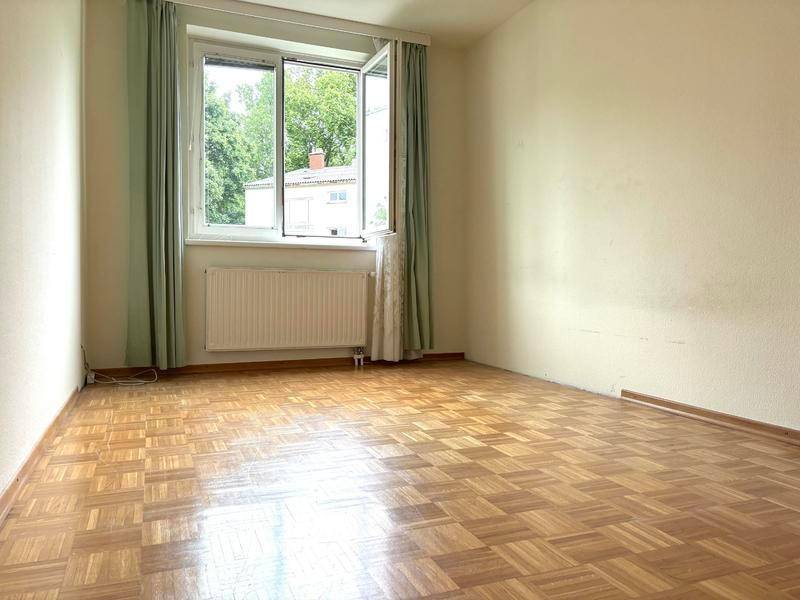 Helles, leeres Zimmer mit Parkettboden und Fenster, ideal als Kinder- oder Arbeitszimmer.