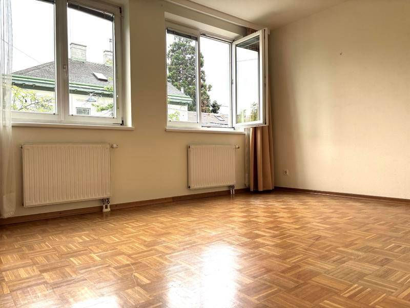 Geräumiger, leerer Raum mit Parkettboden und zwei Fenstern, bietet viel Tageslicht.