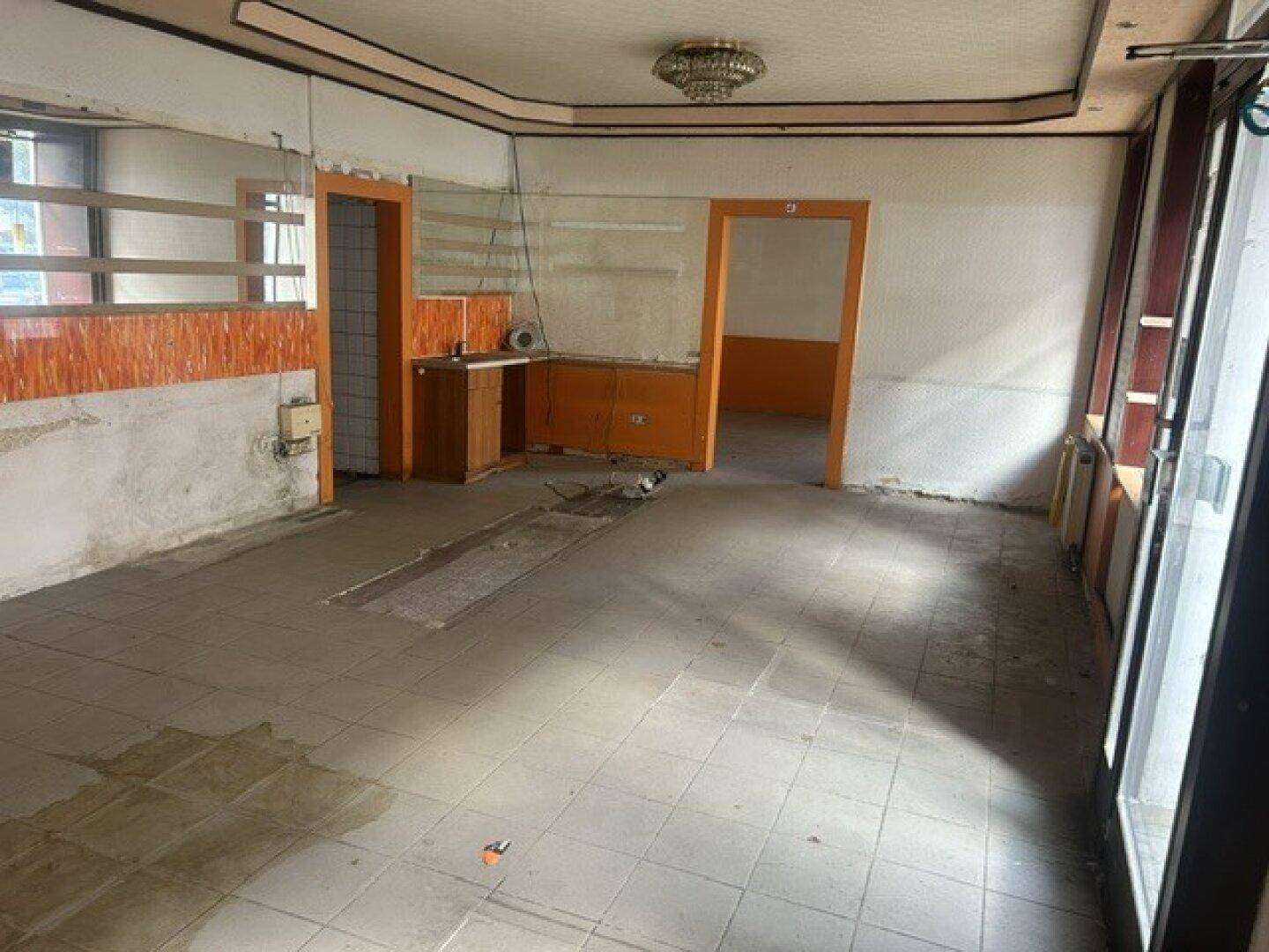 Leerer Innenraum mit Fliesenboden, teilweise abgenutzten Wänden und zwei Türen, bereit zur Renovierung.