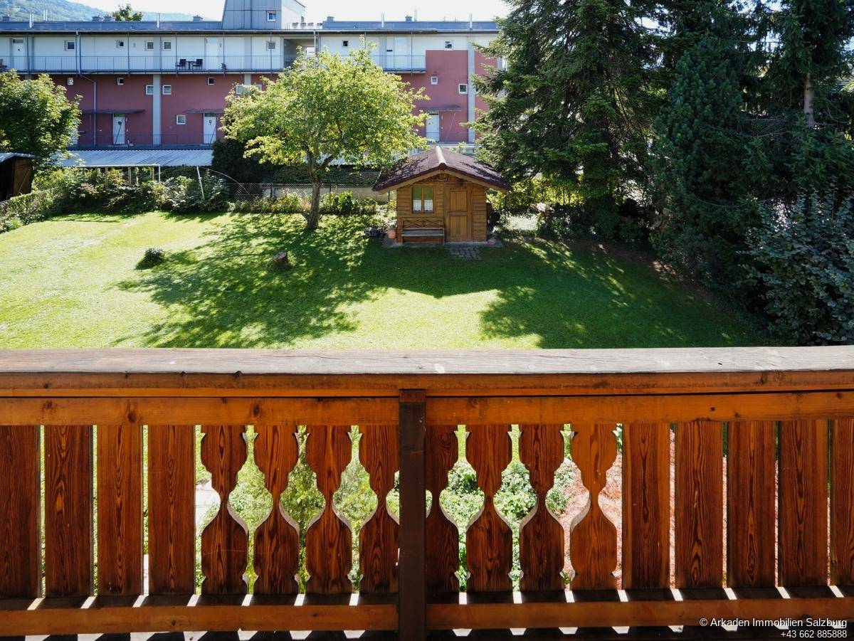 Balkon mit traditionellem Holzgeländer und Blick auf den grünen Garten mit Gartenhaus.