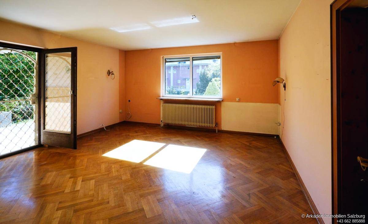Heller Wohnraum mit Fischgrätparkett, großen Fenstern und Zugang zum Außenbereich.