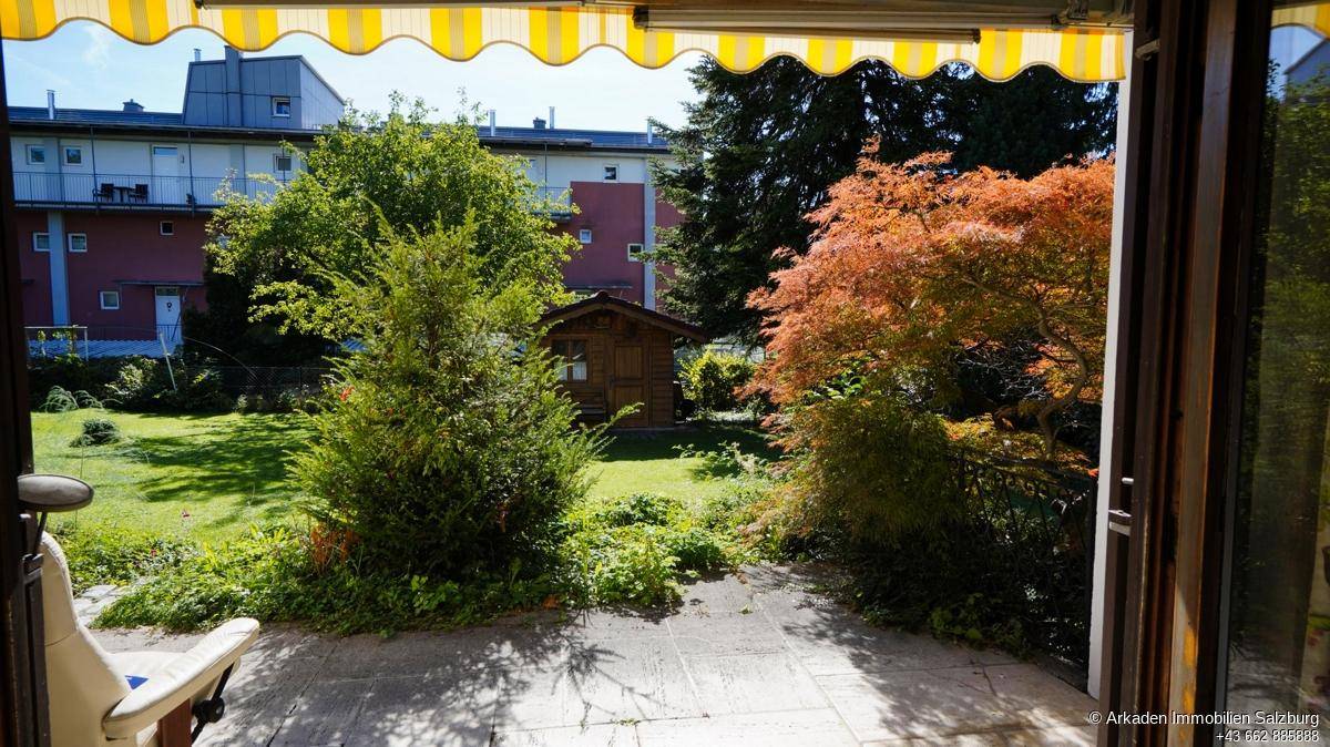 Gemütliche Terrasse mit Markise und Blick auf den gepflegten Garten mit Gartenhaus.