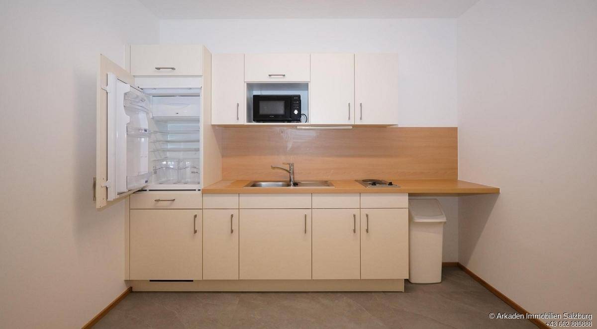 Funktionale Küchenzeile mit geöffnetem Kühlschrank, Mikrowelle und Kochfeld, ideal für kleine Wohnbereiche.