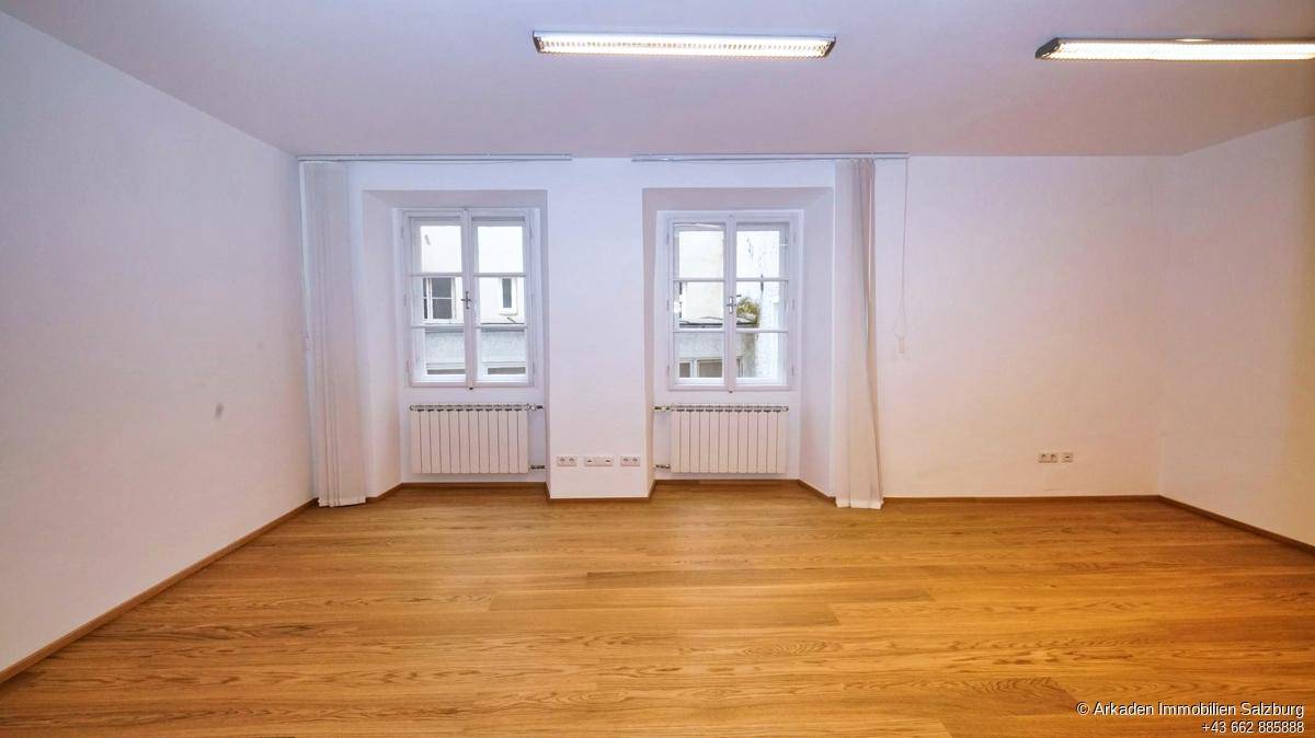 Geräumiger, unmöblierter Raum mit Holzboden, weißen Wänden und zwei Fenstern, die für Helligkeit sorgen.