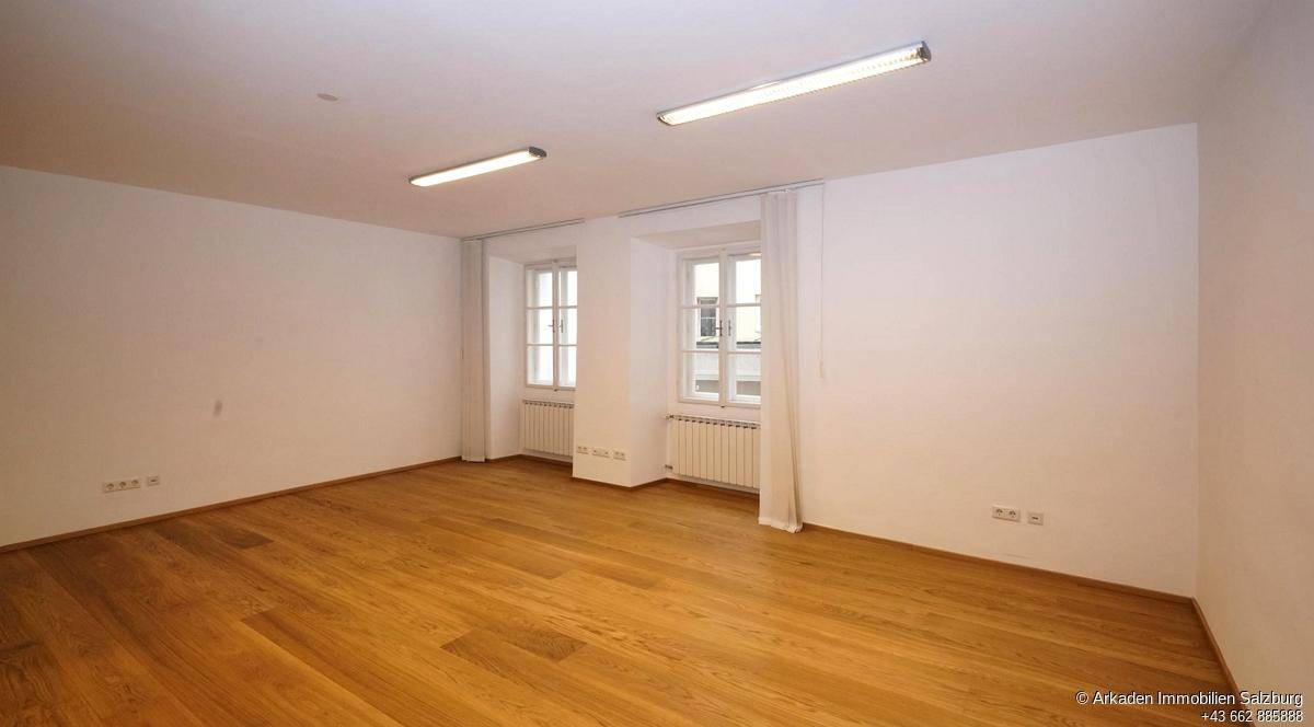 Heller Raum mit warmem Holzboden, weißen Wänden und zwei Fenstern, die eine angenehme Atmosphäre schaffen.