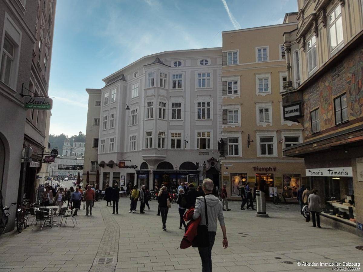 Eine belebte historische Straße mit traditionellen Gebäuden und Passanten unter einem blauen Himmel.