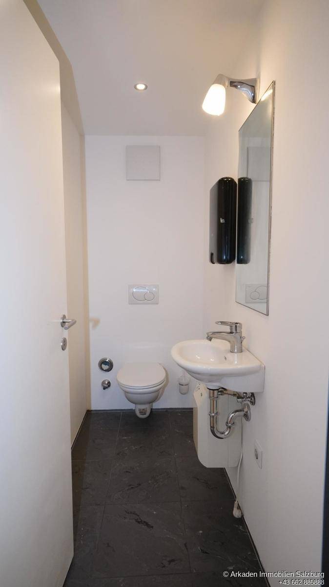 Modernes Gäste-WC mit dunklem Fliesenboden, wandhängendem WC und kleinem Waschbecken mit Spiegel.
