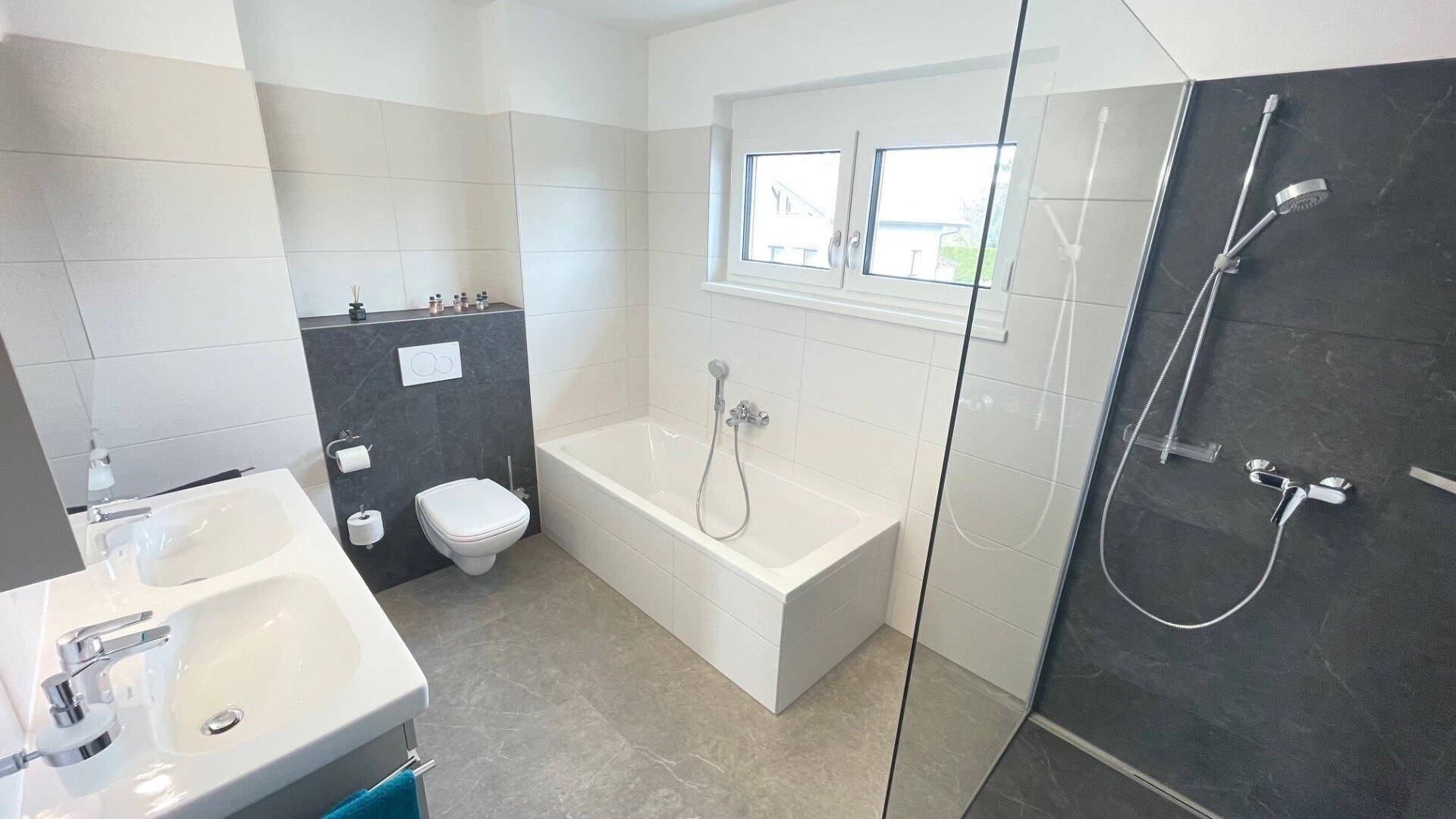 Modernes Badezimmer mit Doppelwaschbecken, Badewanne, Dusche und Fenster für natürliches Licht.