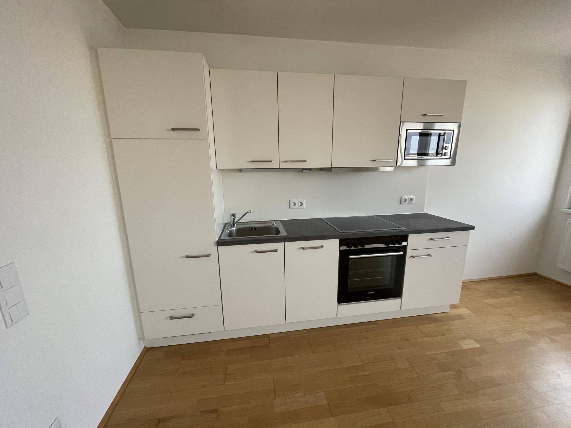 Moderne Einbauküche mit weißen Schränken, dunkler Arbeitsplatte und integrierten Geräten.