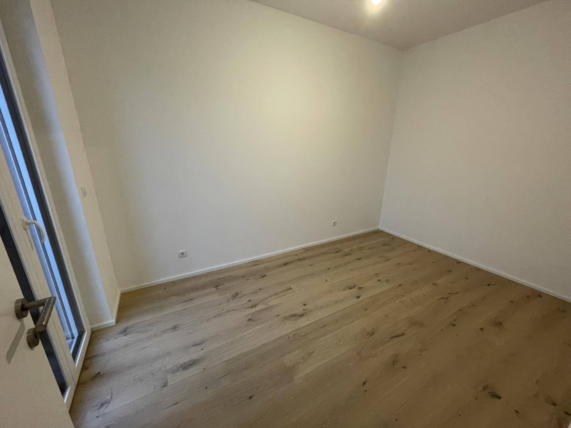 Leeres Zimmer mit Holzboden und Zugang zu einem französischen Balkon, bietet einen Blick auf die Stadt.