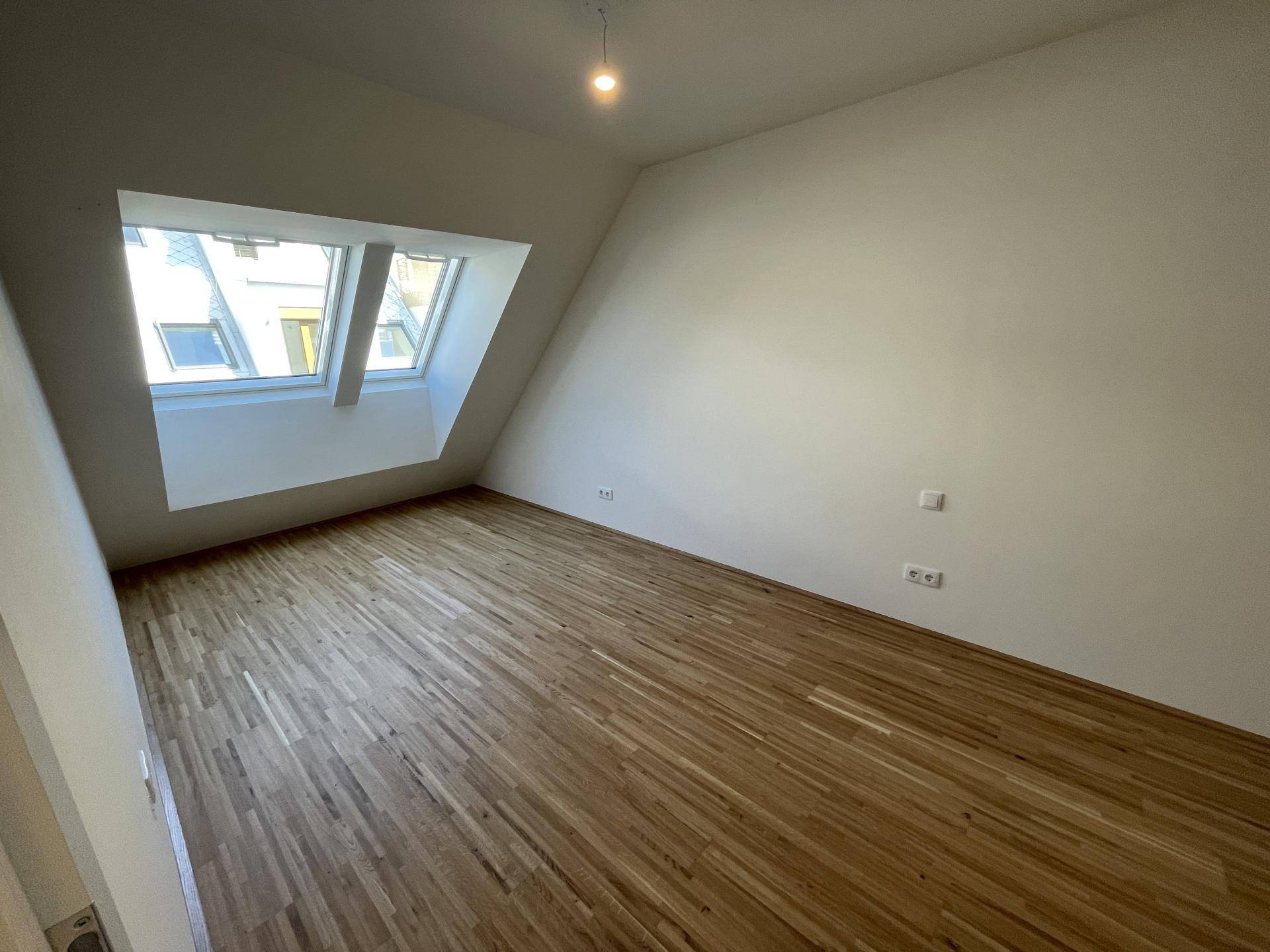 Geräumiges Zimmer mit Holzboden, Dachschrägen und hellen Dachfenstern.