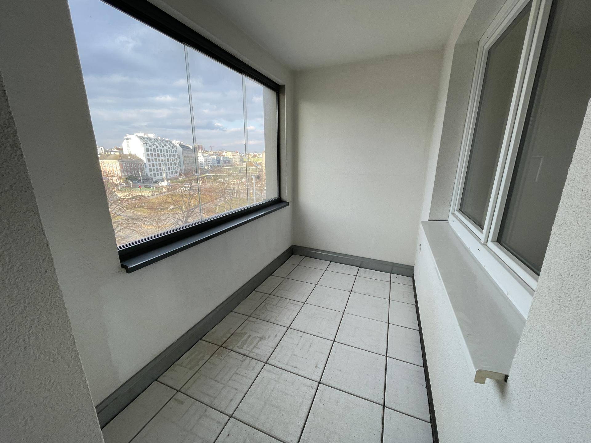 Verglaster Balkon mit Fliesenboden und Blick auf die Stadt.