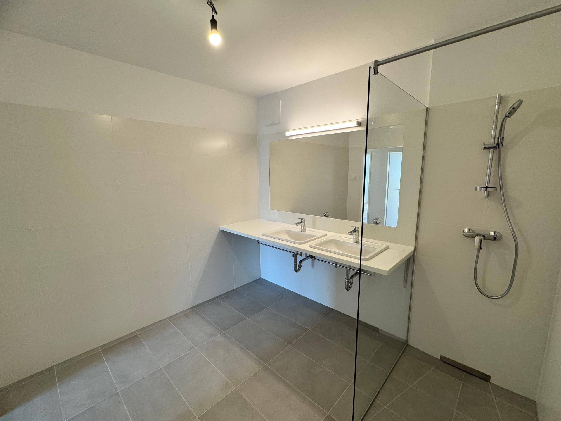 Helles Badezimmer mit Doppelwaschbecken, großer begehbarer Dusche und Fliesenboden.