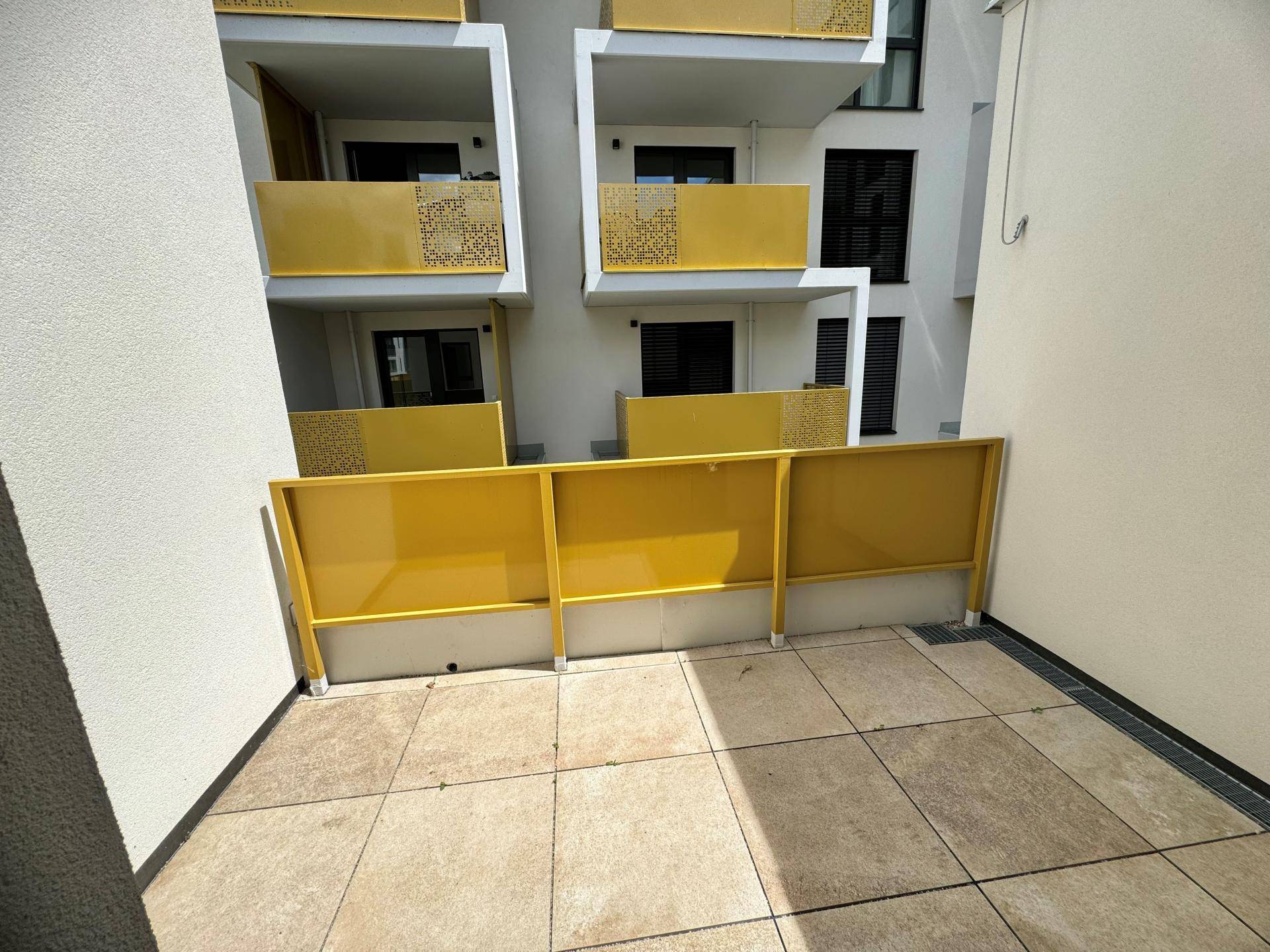 Private Terrasse mit Fliesenboden und gelben Sichtschutzelementen, umgeben von modernen Gebäuden.