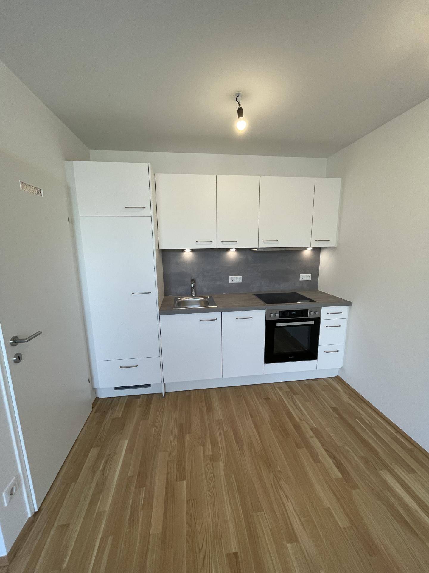 Moderne, kompakte Einbauküche mit weißen Schränken, integrierten Geräten und Holzparkettboden.