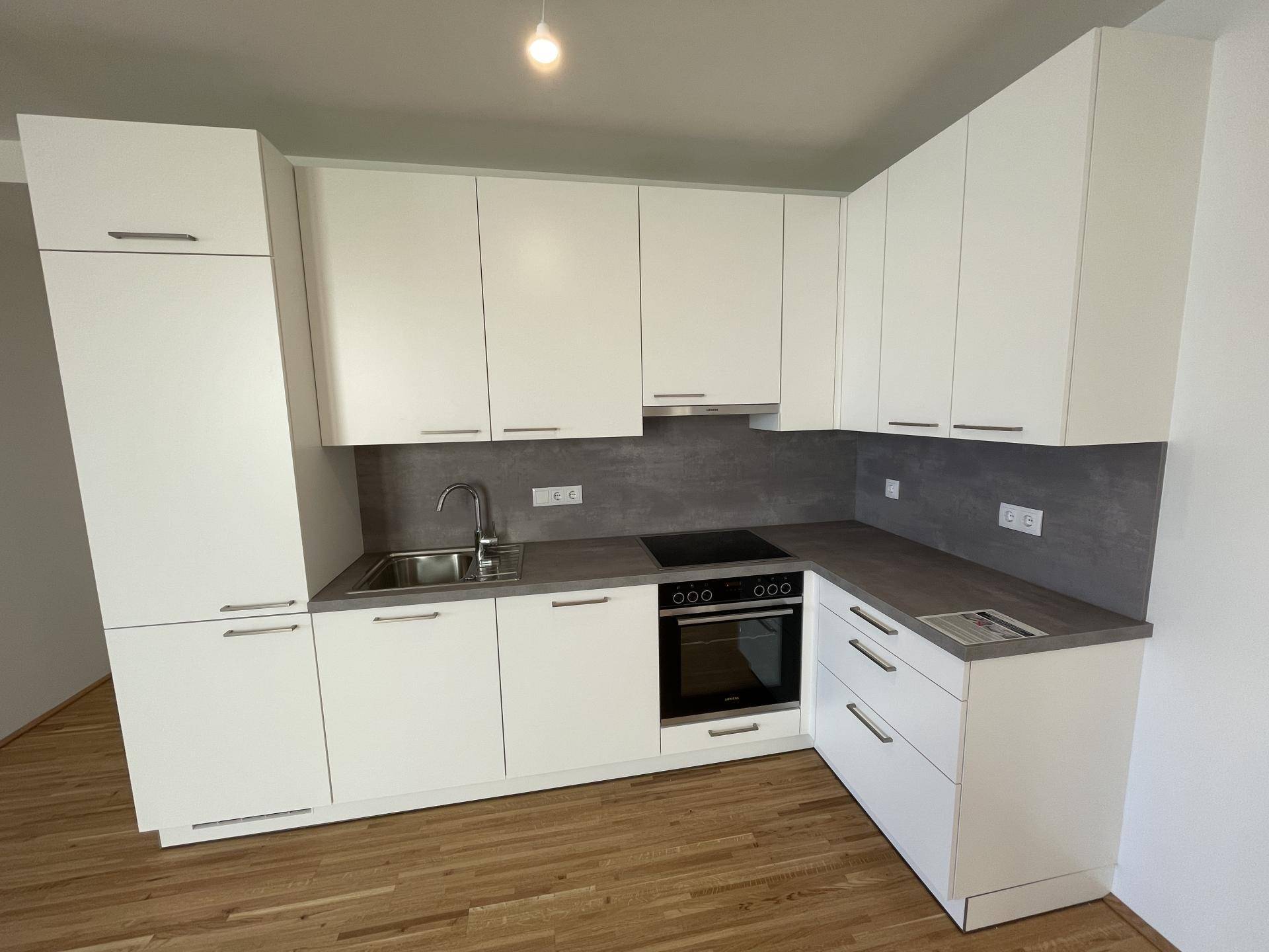 Moderne Einbauküche mit weißen Schränken, dunkler Arbeitsplatte und integrierten Geräten.