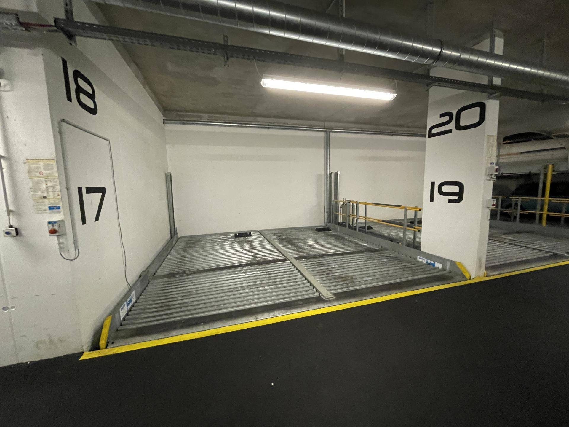 Tiefgaragenstellplatz mit nummerierten Parkplätzen und mechanischem Doppelparker in sauberem Zustand.