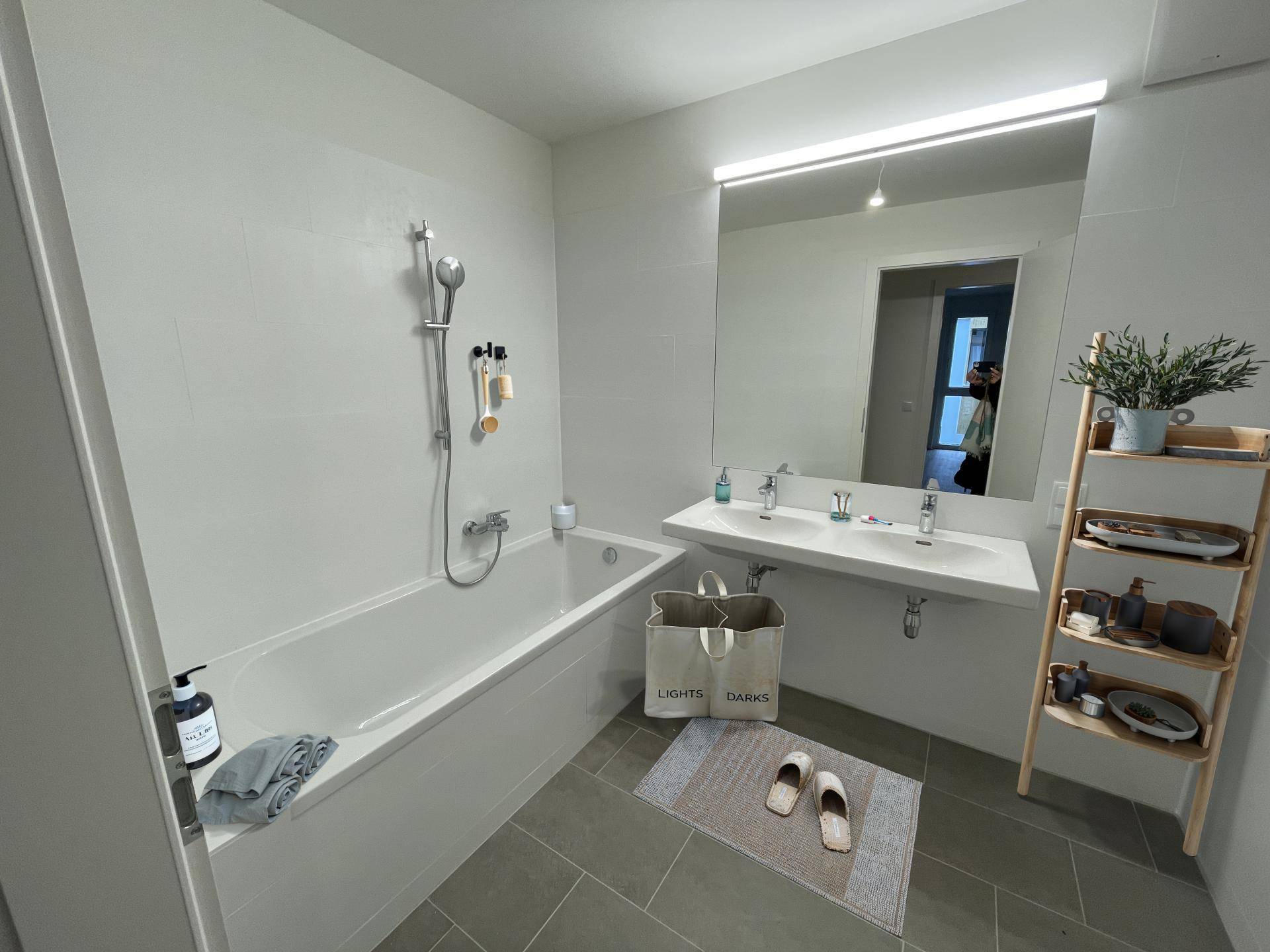 Modernes Badezimmer mit Badewanne, Doppelwaschbecken und großen hellgrauen Fliesen.