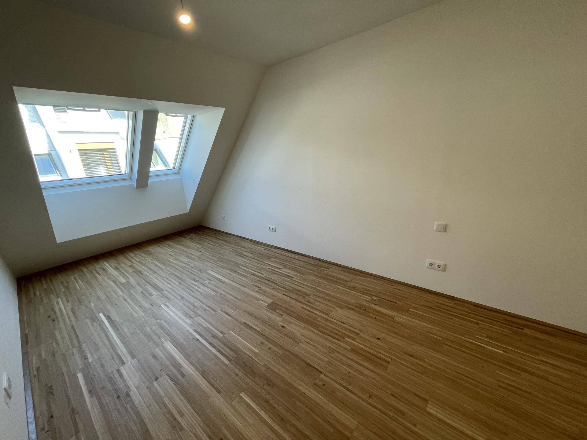 Helles Zimmer mit Holzboden und Dachfenster, bietet eine gemütliche Atmosphäre unter dem Dach.
