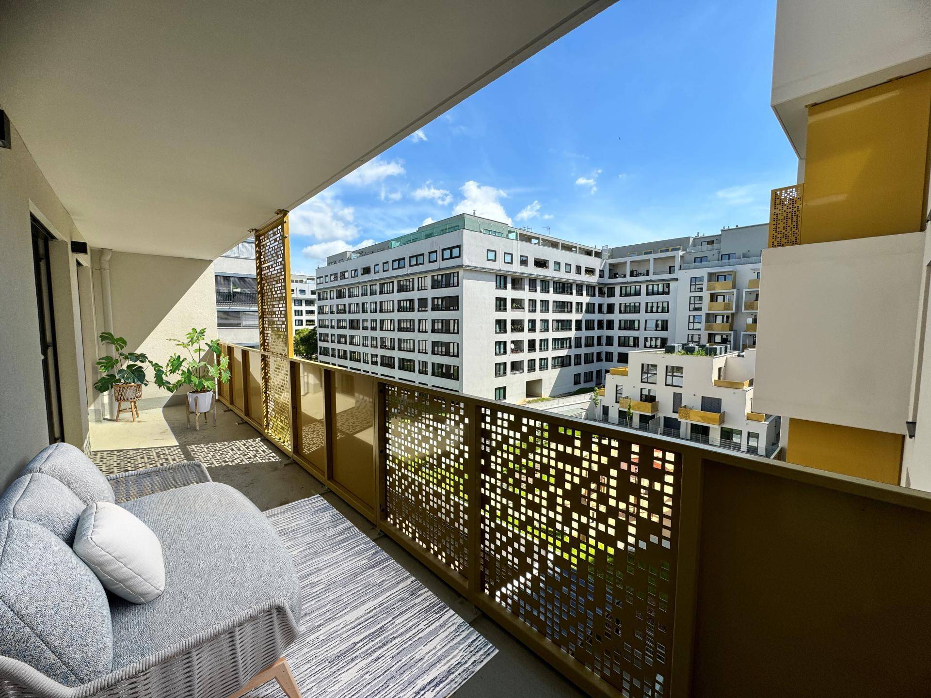 Geräumiger Balkon mit Sitzgelegenheiten und Blick auf die umliegenden Gebäude, sonnig und modern.
