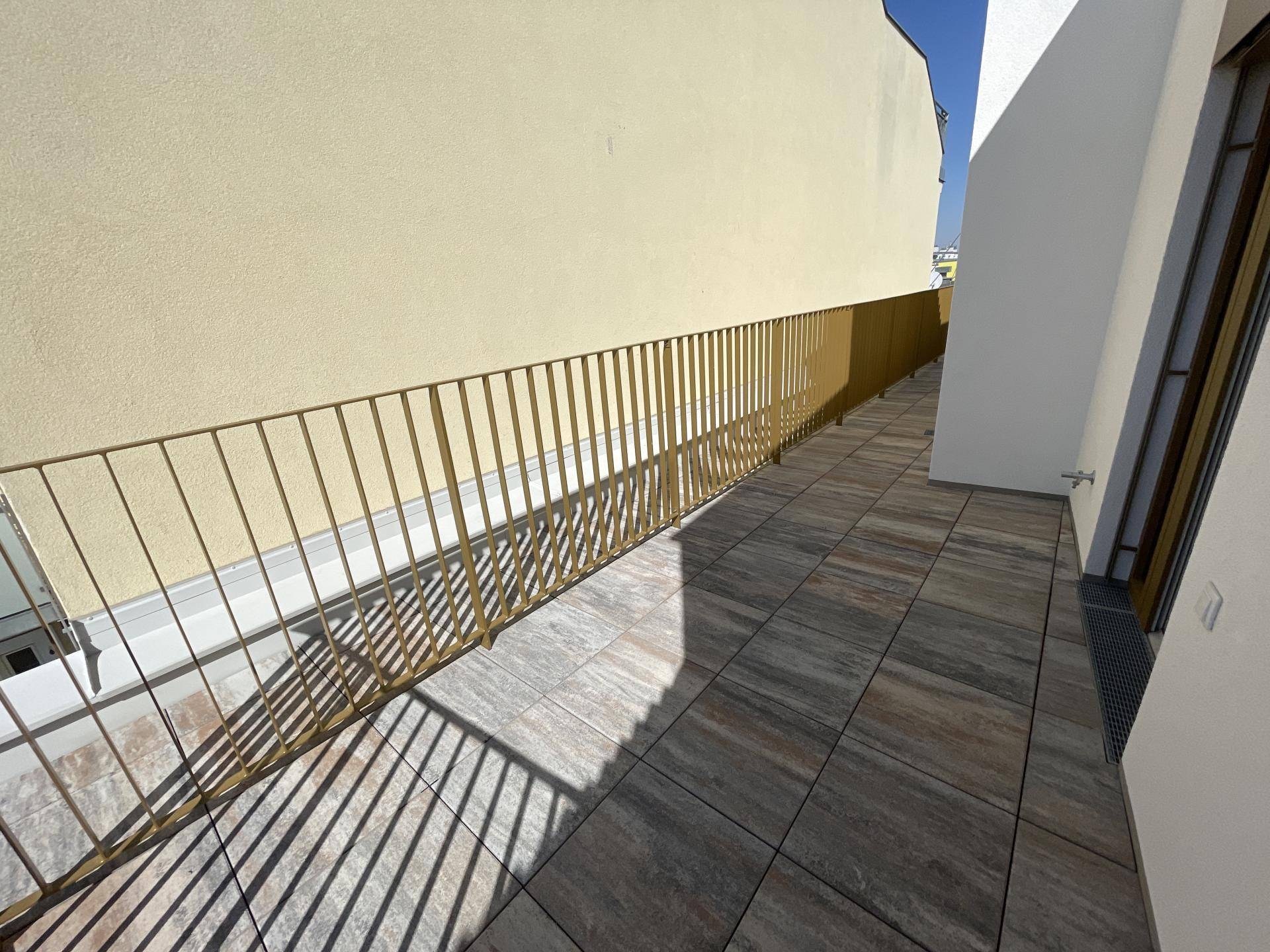 Langer, schmaler Balkon mit Fliesenboden und goldener Metallbrüstung, sonnig gelegen.