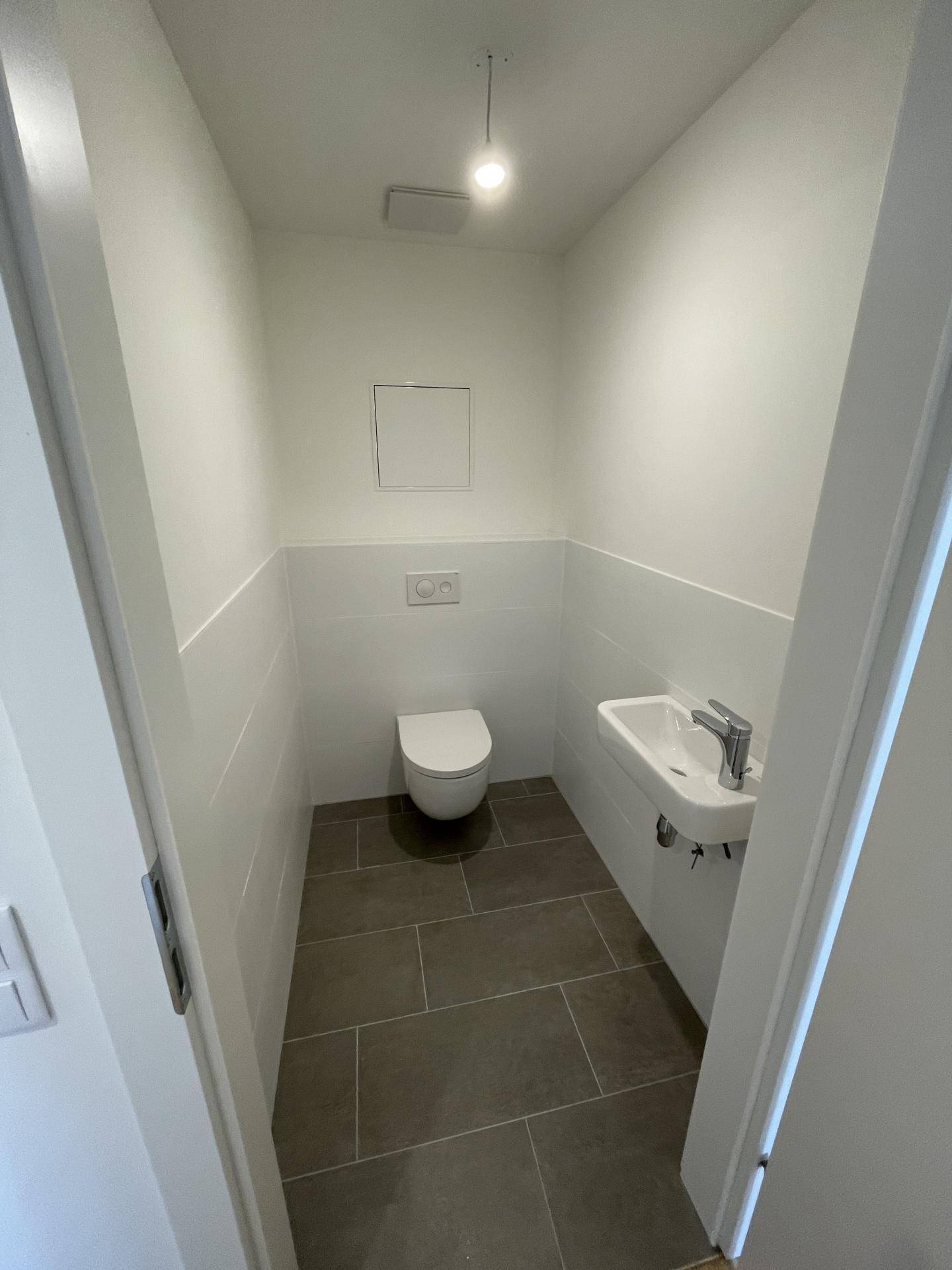 Modernes Gäste-WC mit wandhängender Toilette und kleinem Waschbecken, in neutralen Farben gehalten.