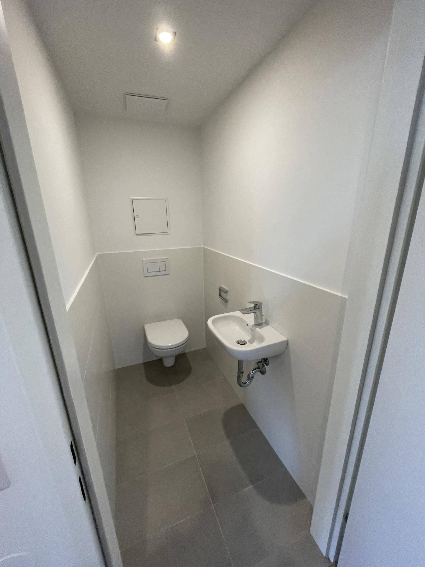 Separates Gäste-WC mit wandhängender Toilette und kleinem Handwaschbecken, modern gefliest.