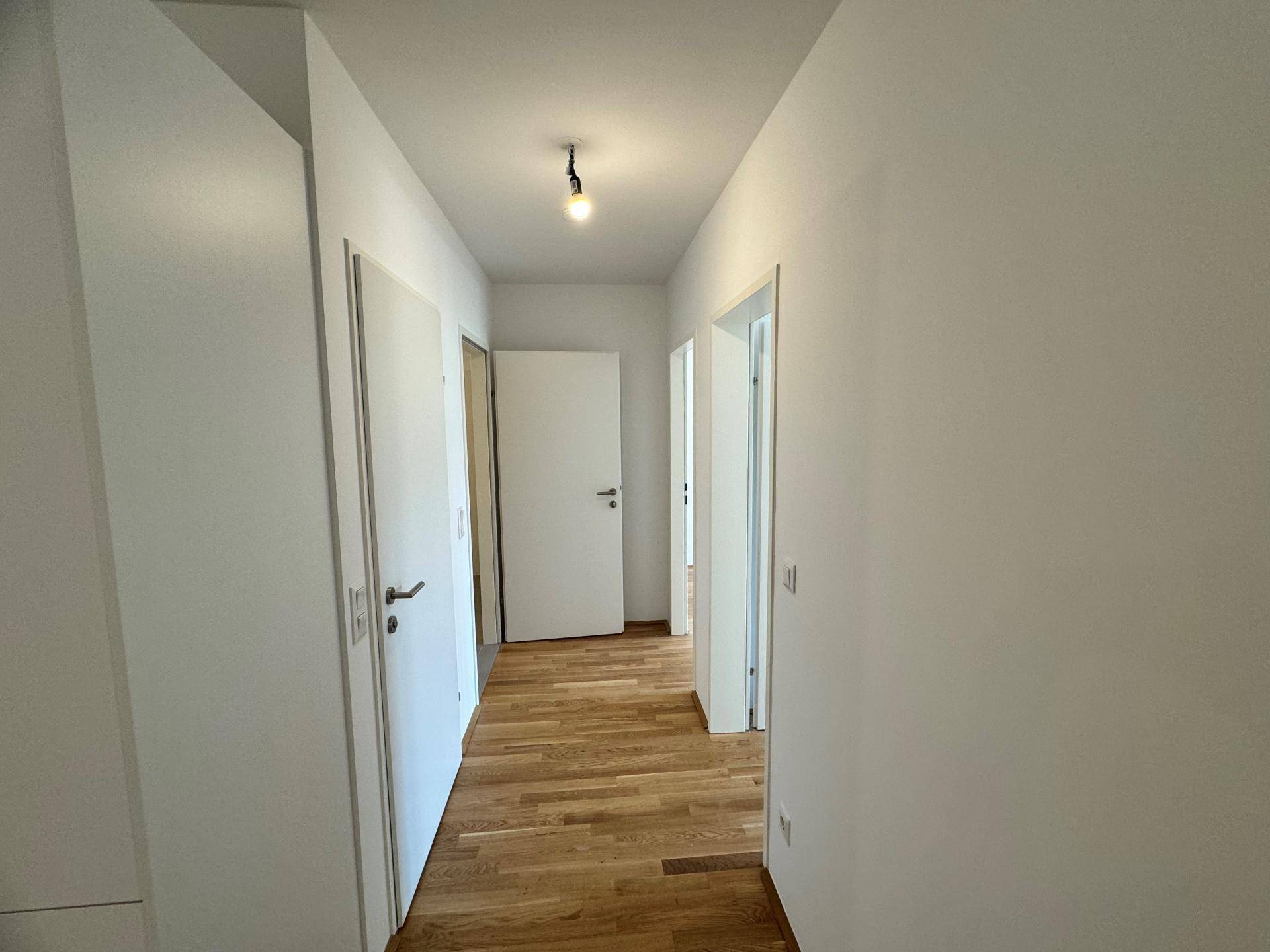 Heller Flur mit Parkettboden und weißen Wänden, der zu weiteren Räumen führt.