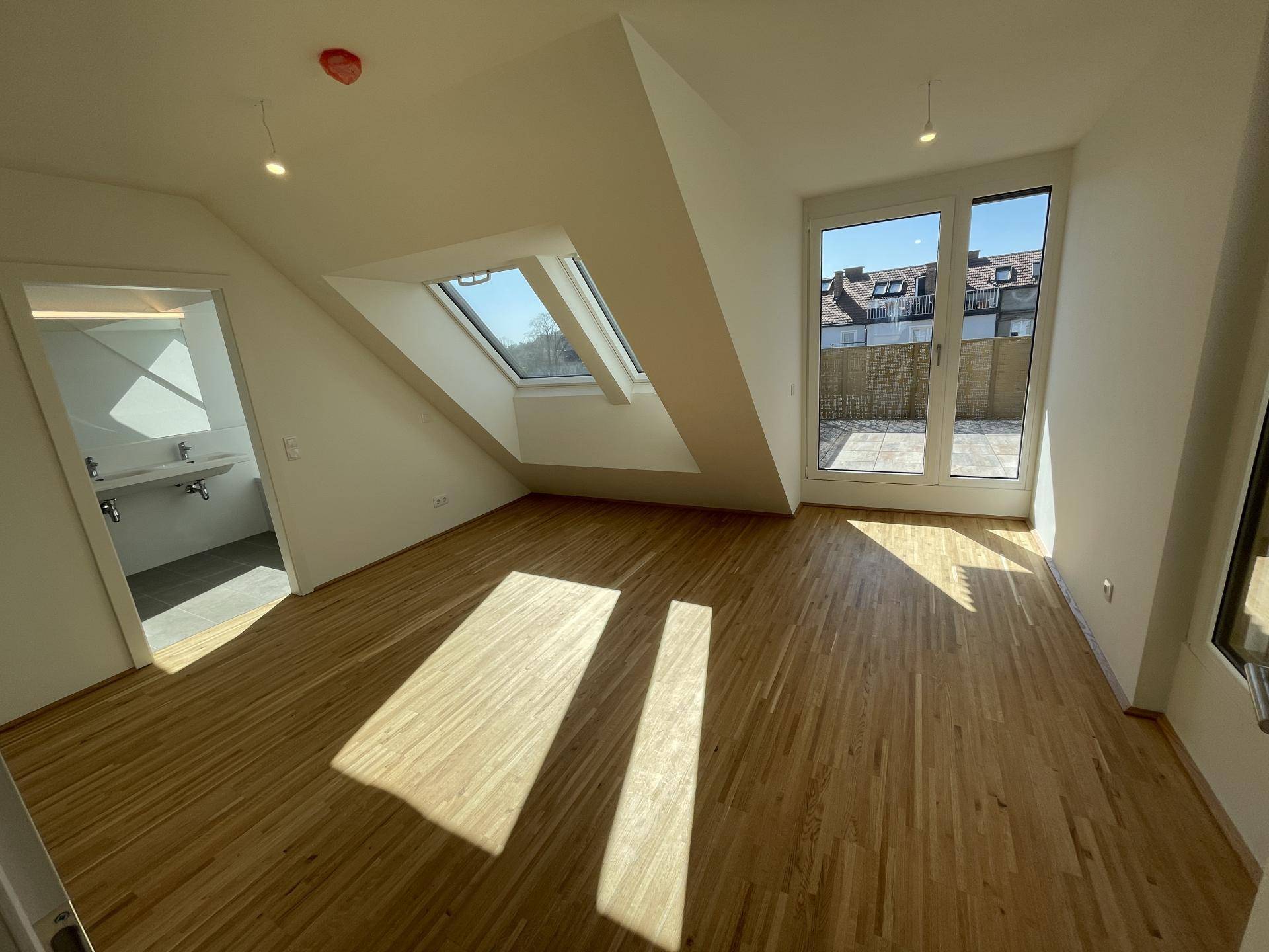 Geräumiges Zimmer mit Parkettboden, Dachfenstern und Zugang zu einem Außenbereich.