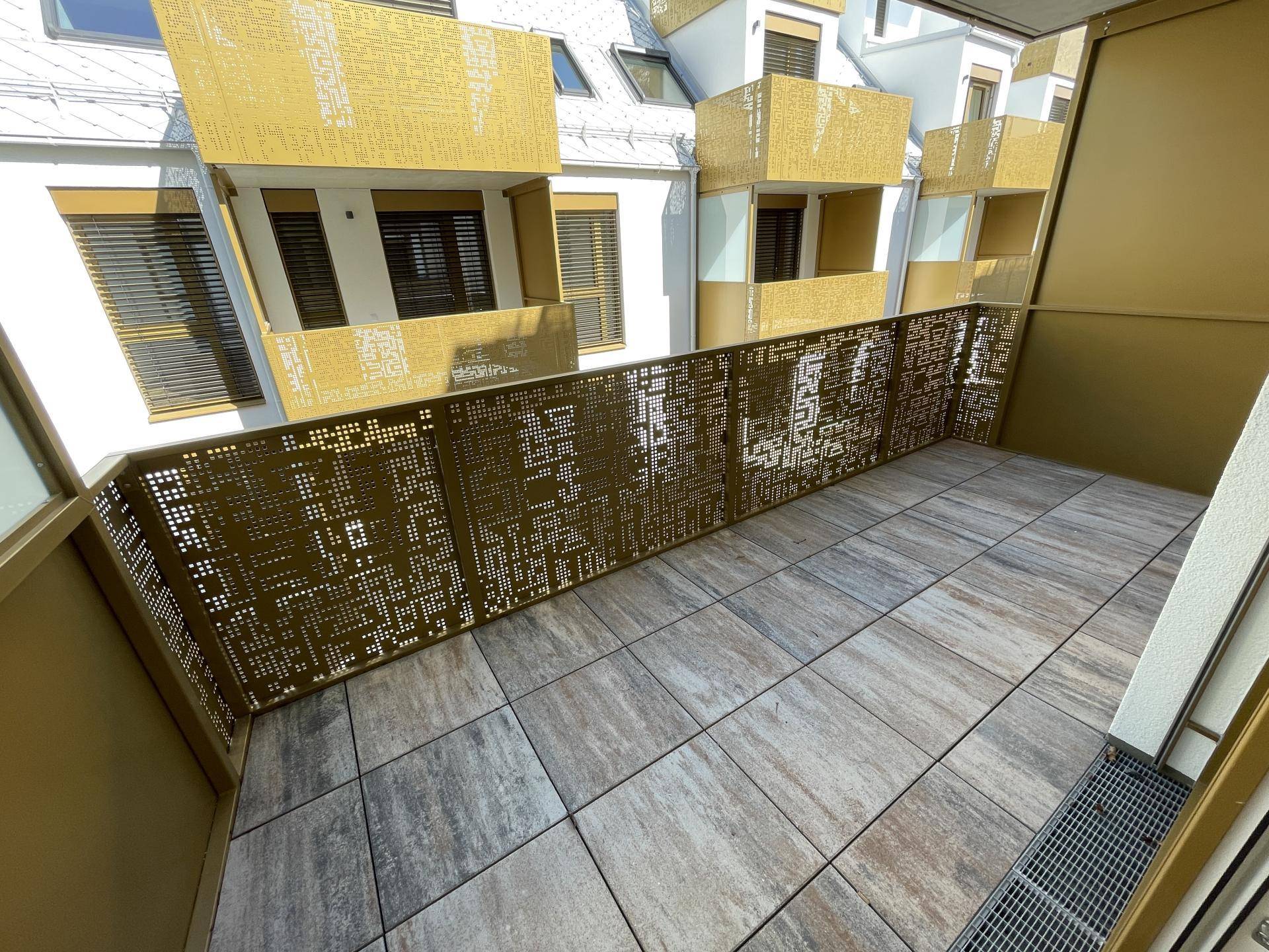 Geräumiger Balkon mit Fliesenboden und modernem, dekorativem Geländer in Goldtönen.