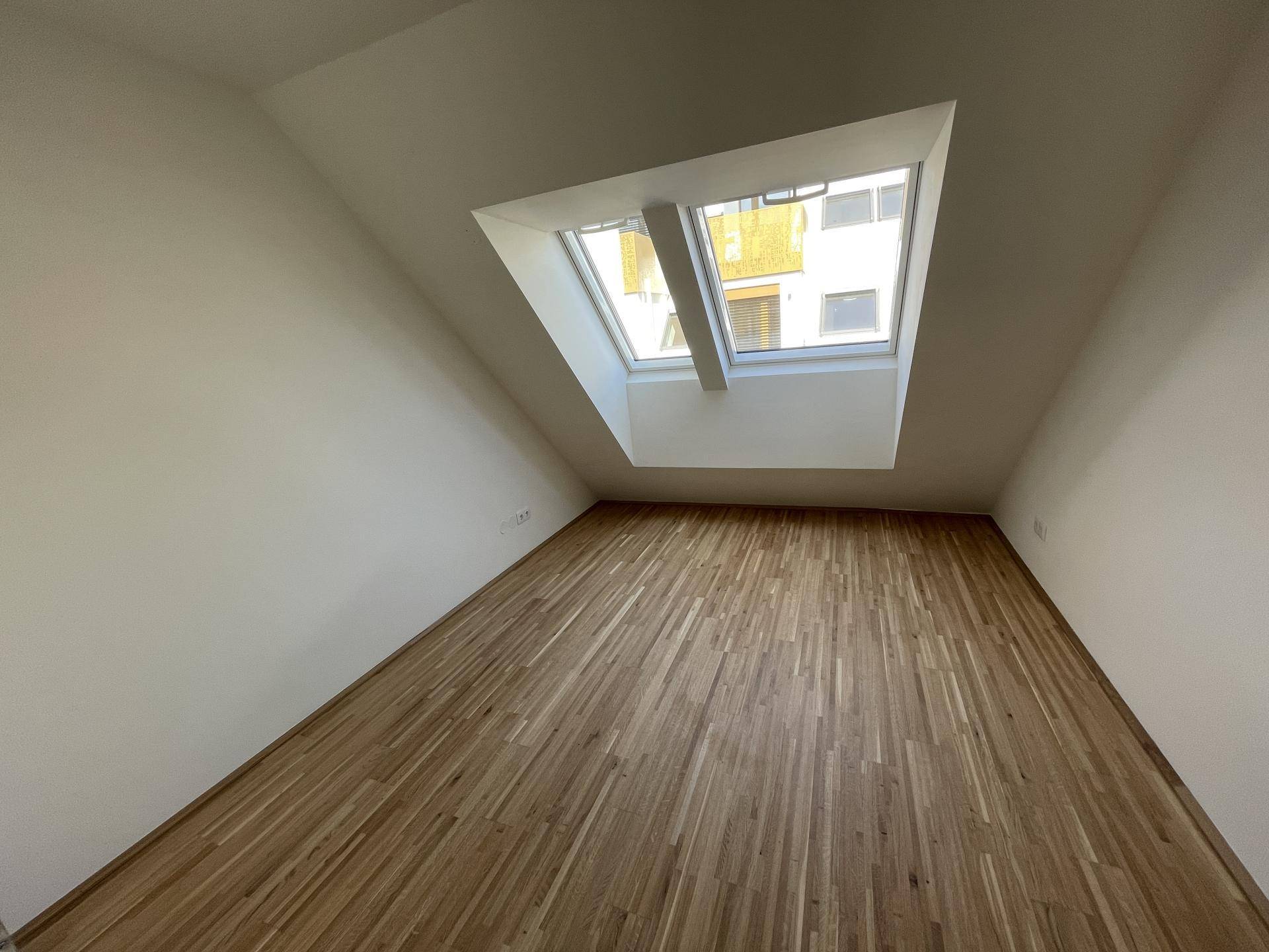 Gemütliches Zimmer mit Holzboden und großem Dachfenster, sorgt für viel Tageslicht.