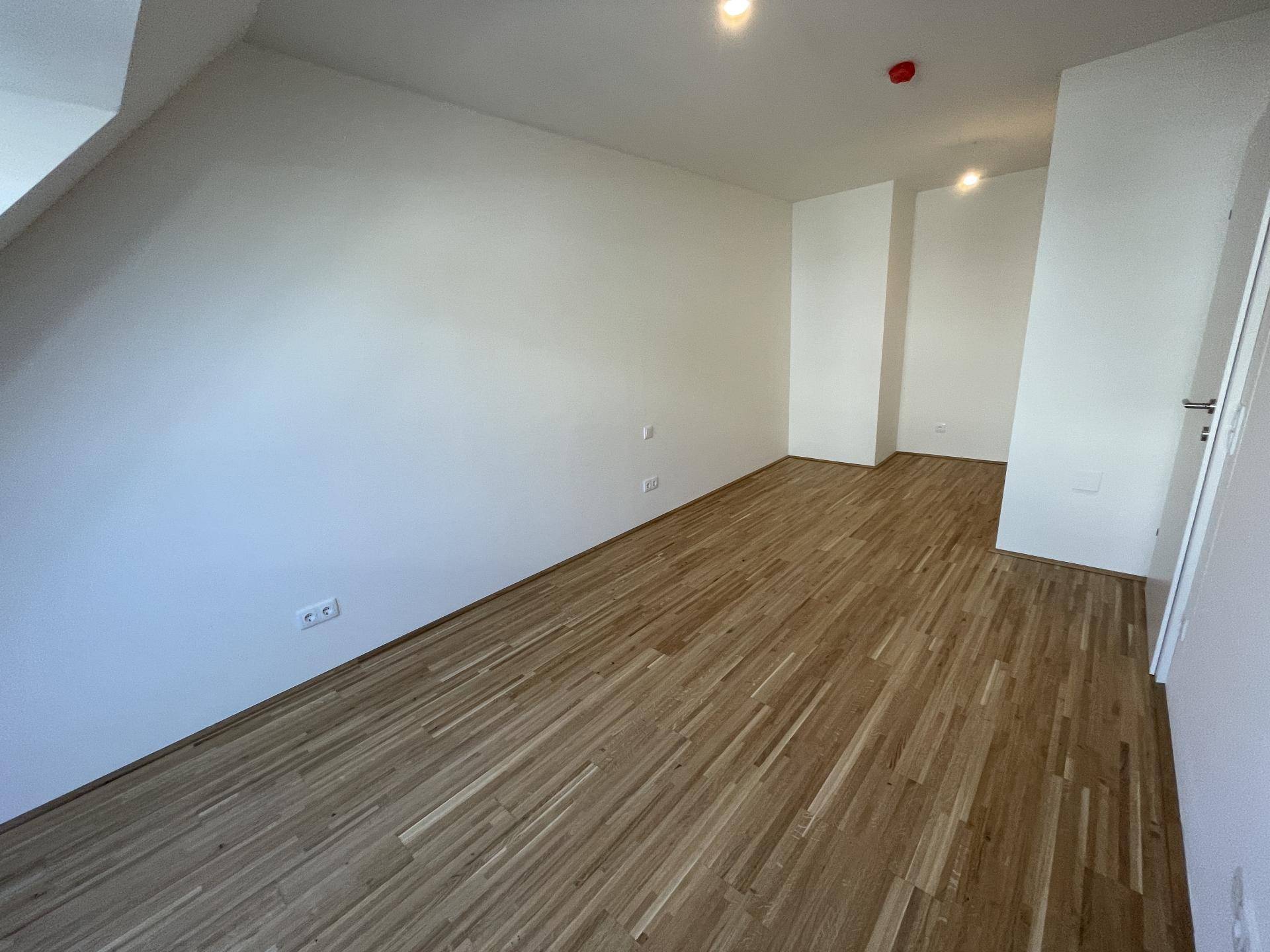 Leerer Raum mit Holzboden und schrägen Wänden, bietet Flexibilität für verschiedene Nutzungen.