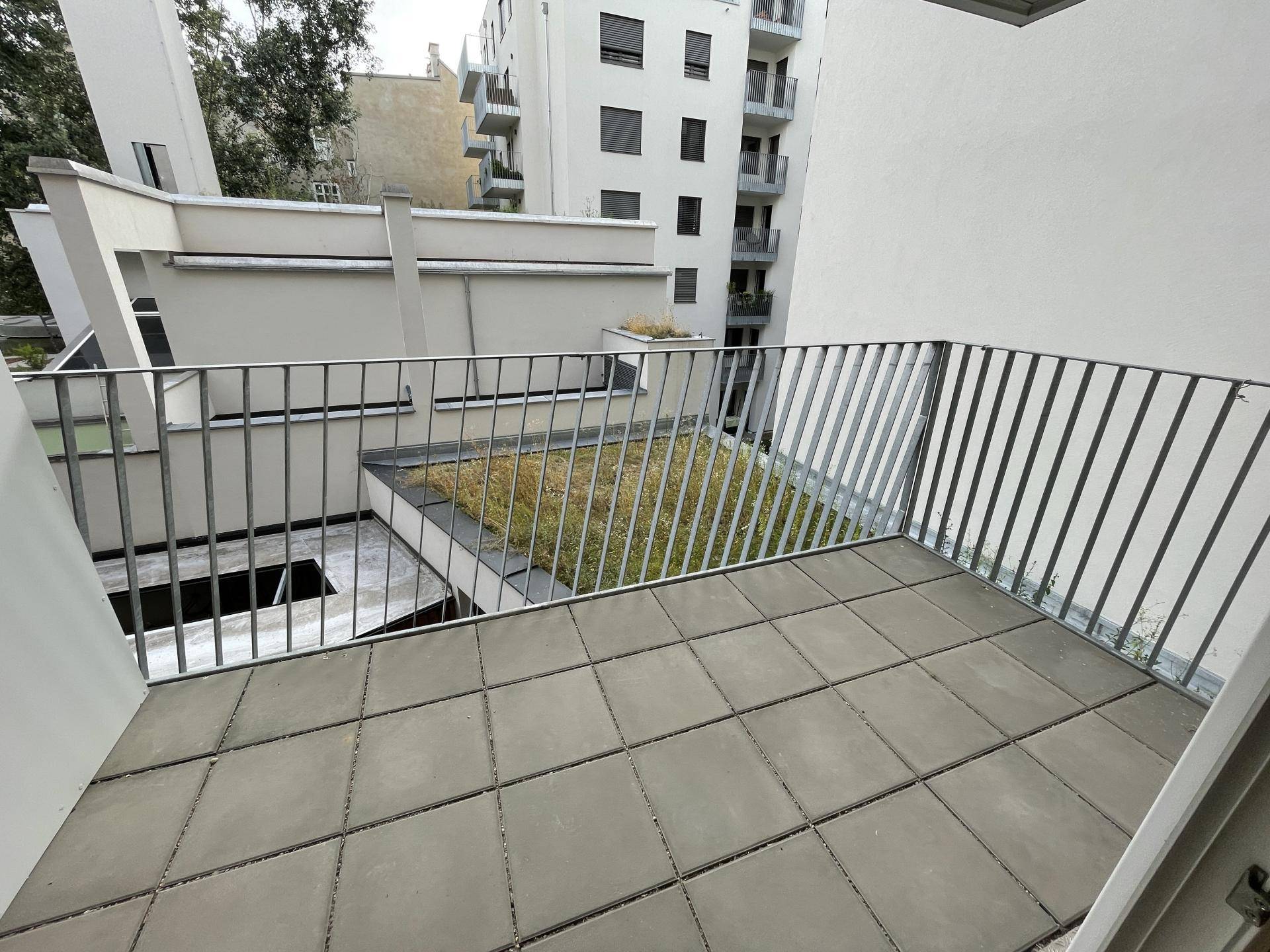 Kleiner Balkon mit Fliesenboden und Metallgeländer, bietet einen Blick auf die umliegenden Gebäude.