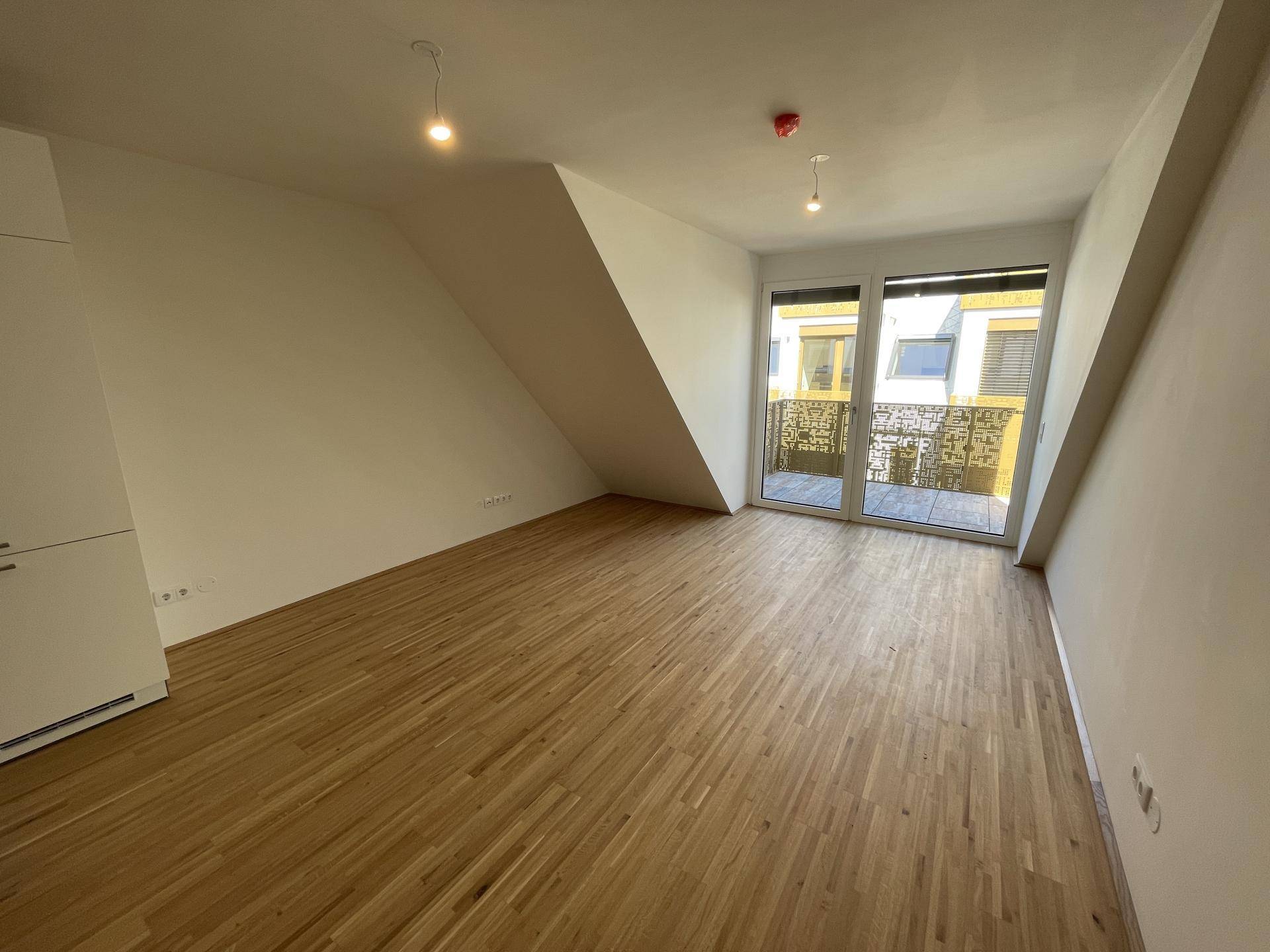 Geräumiger Raum mit Holzboden und Zugang zu einem Balkon, bietet viel natürliches Licht.