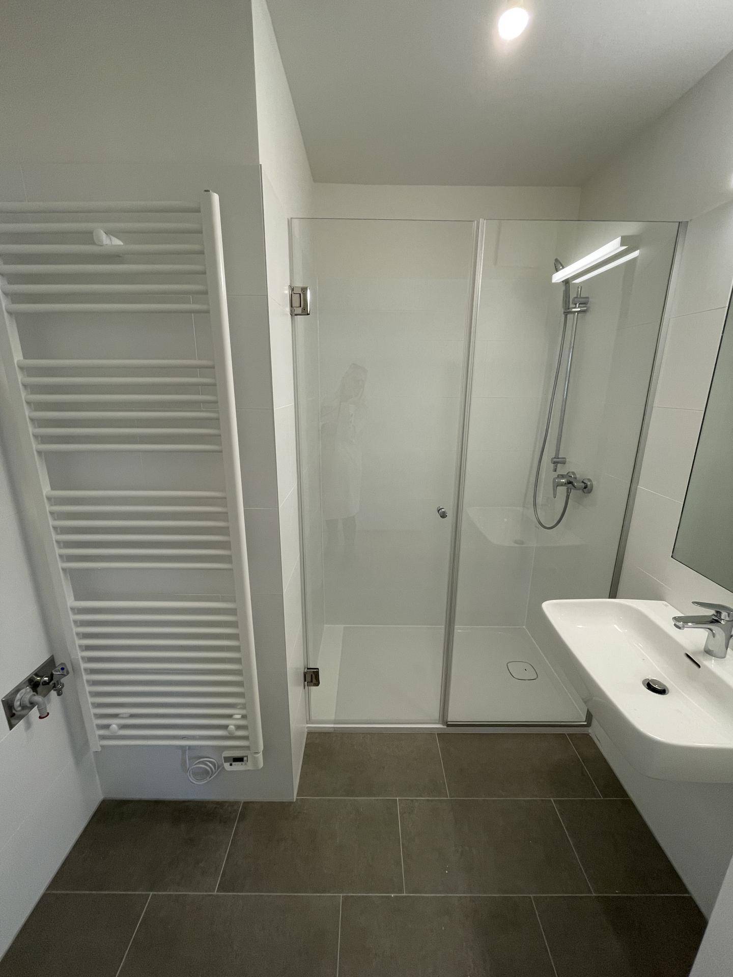 Modernes Badezimmer mit Dusche, Waschbecken, beheiztem Handtuchhalter und grauen Fliesen.