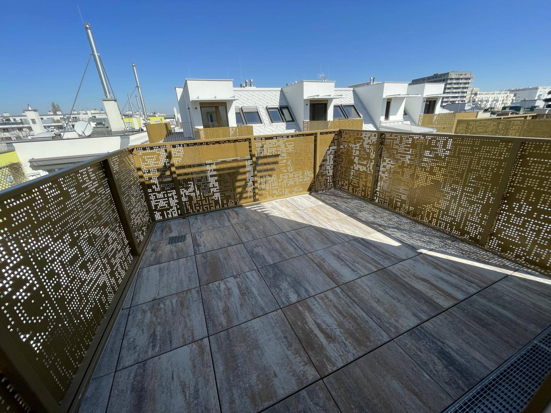Weitläufige Dachterrasse mit modernen Fliesen und dekorativer Metallbrüstung, unter blauem Himmel.