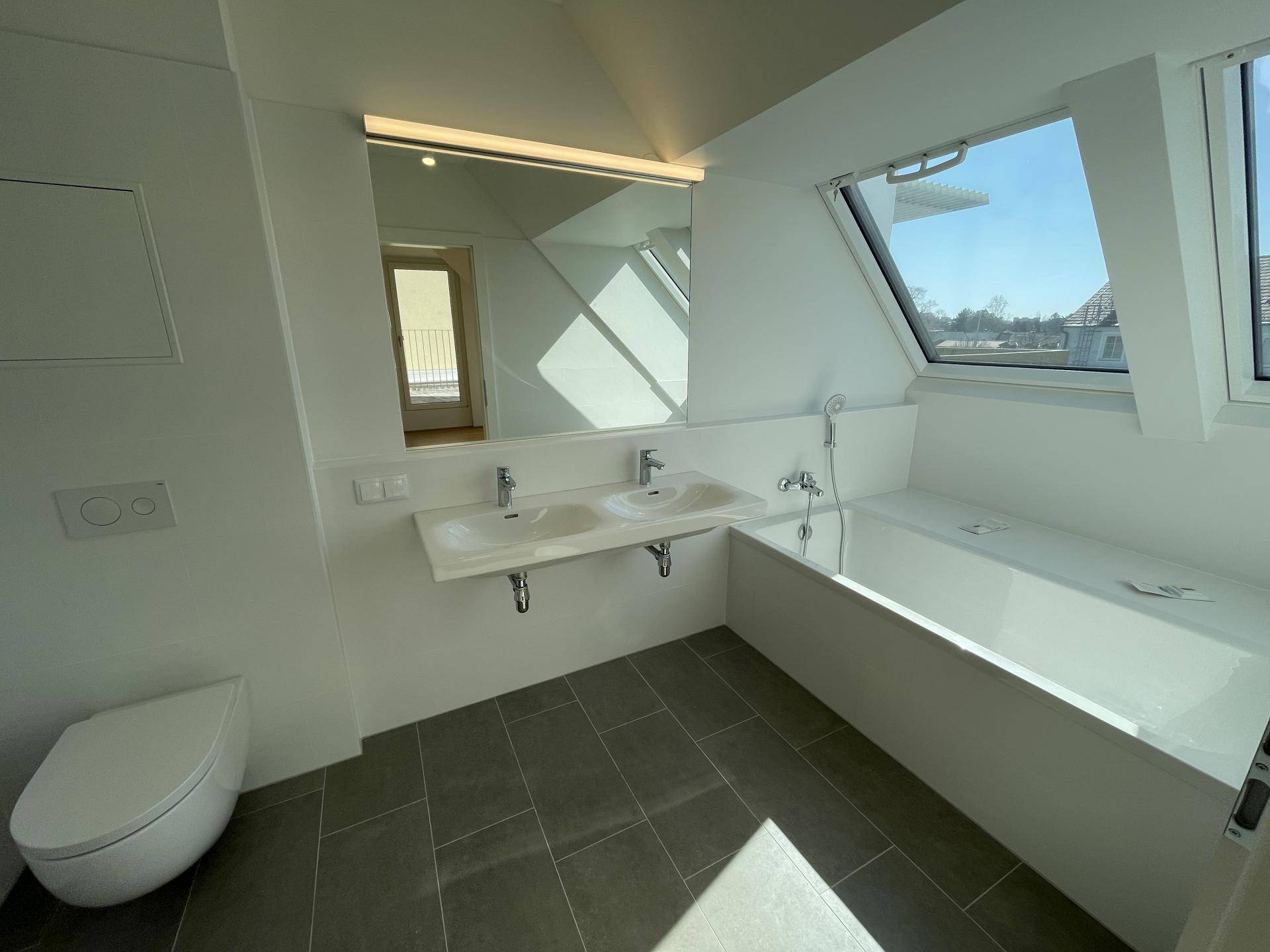 Modernes Badezimmer mit Doppelwaschbecken, Badewanne, WC und Dachfenstern für Tageslicht.