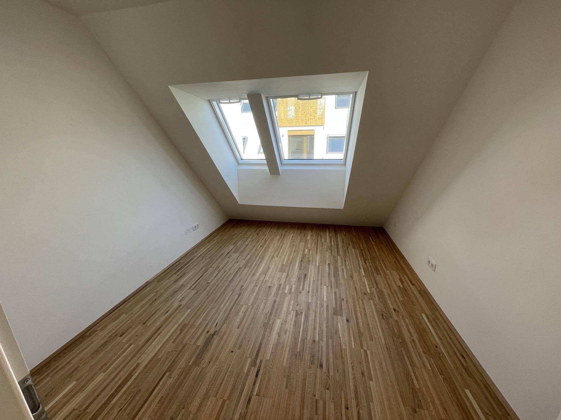 Helles Zimmer mit Holzboden, Dachschrägen und großen Dachfenstern für viel Tageslicht.