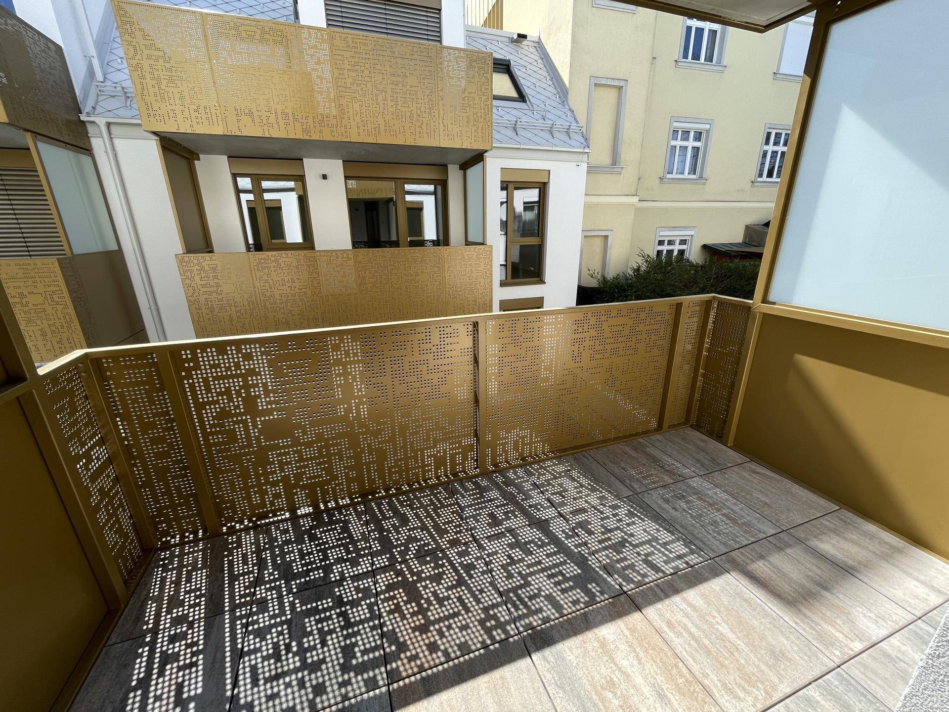 Moderner Balkon mit perforiertem Metallgeländer und Fliesenboden, der interessante Schatten wirft.
