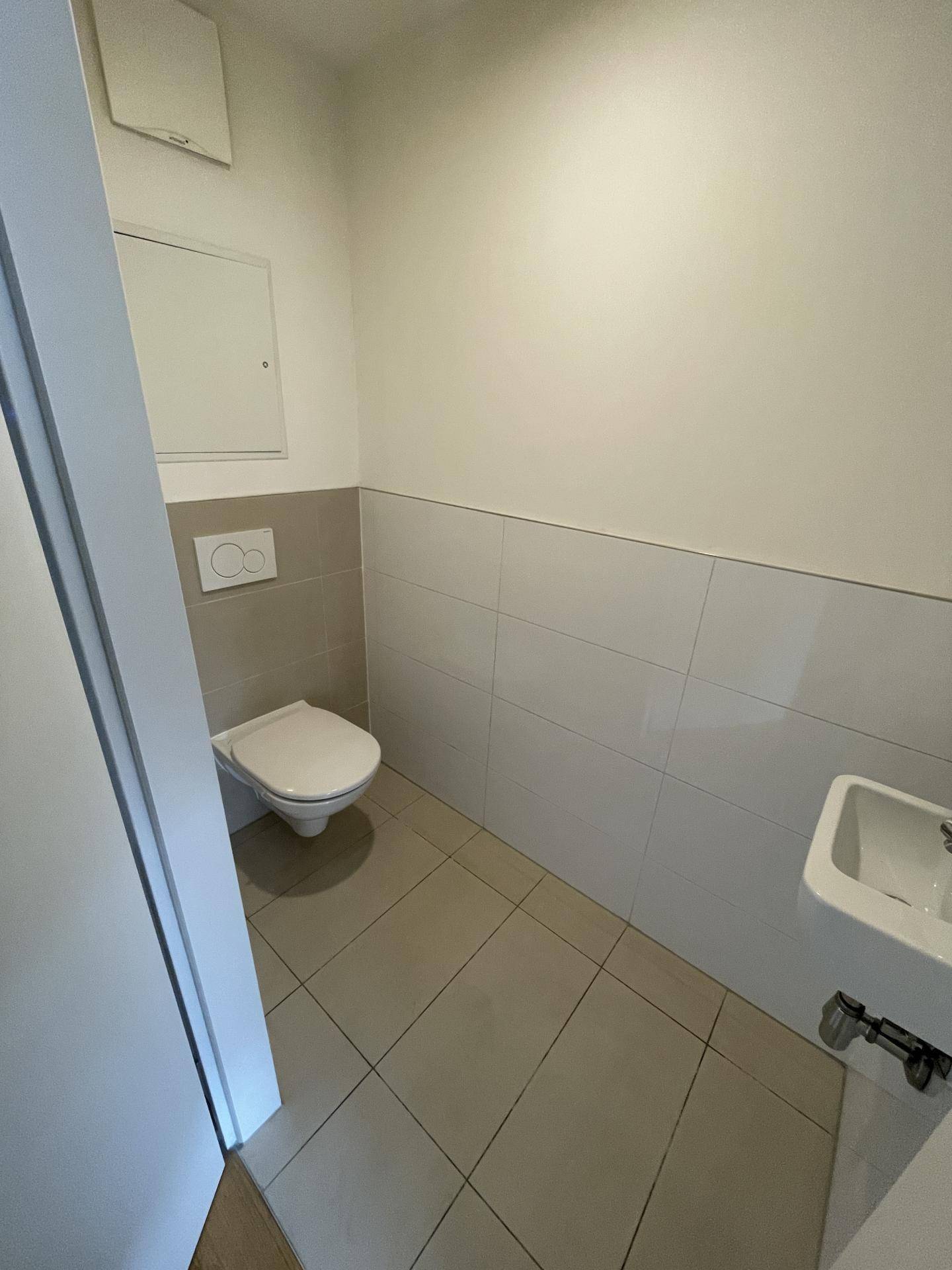 Separates Gäste-WC mit wandhängender Toilette und kleinem Handwaschbecken.