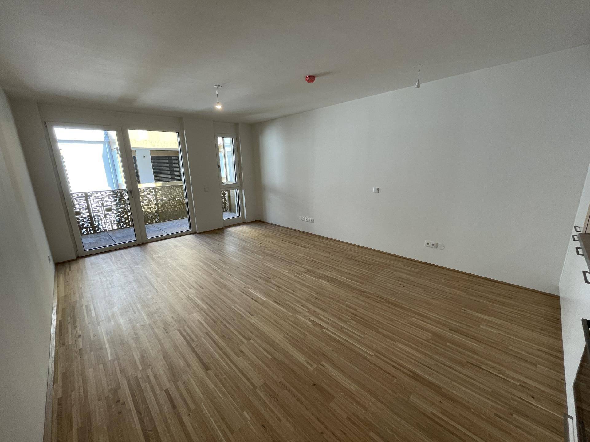 Geräumiges Wohnzimmer mit hellem Parkettboden und direktem Zugang zu einem Balkon, bietet viel Tageslicht.